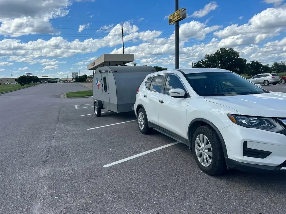 White Nissan Rogue Tow a small camper Trailer